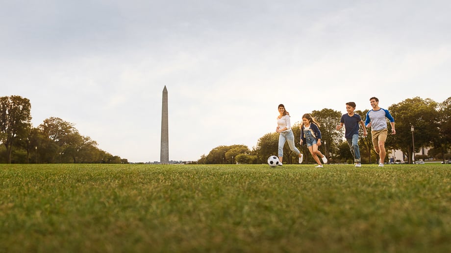 Photo of a family playing football in a field with the Washington Monument in the background taken by Washington DC-based lifestyle photographer Shawn Hubbard. 