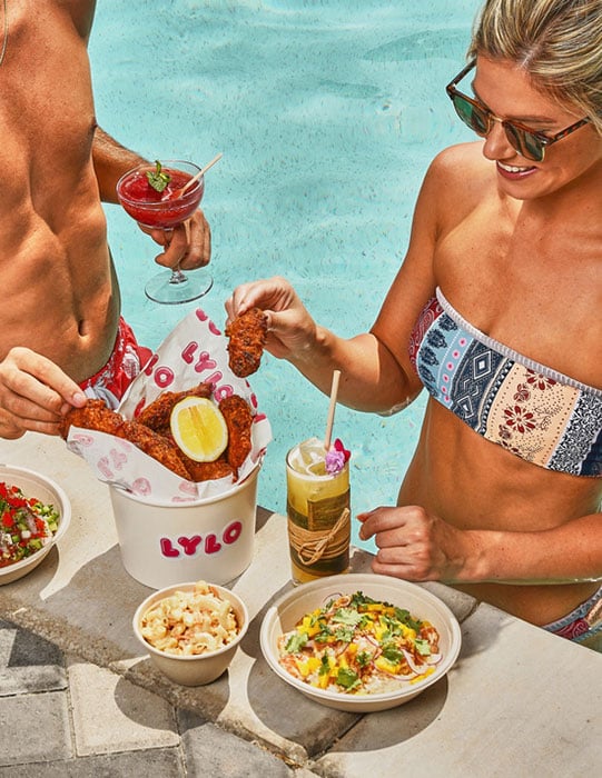 Photo of a man and woman poolside eating Lylo fried chicken taken by Los Angeles-based food photographer Shelby Moore.
