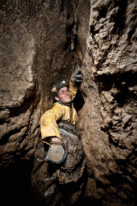 Image of a man in safety gear crawling through a tight spot by adventure photographer Christopher Beauchamp.