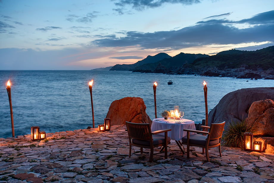Table and chairs surrounded by tiki tourches overlooking the water on Vietnam's coastline.