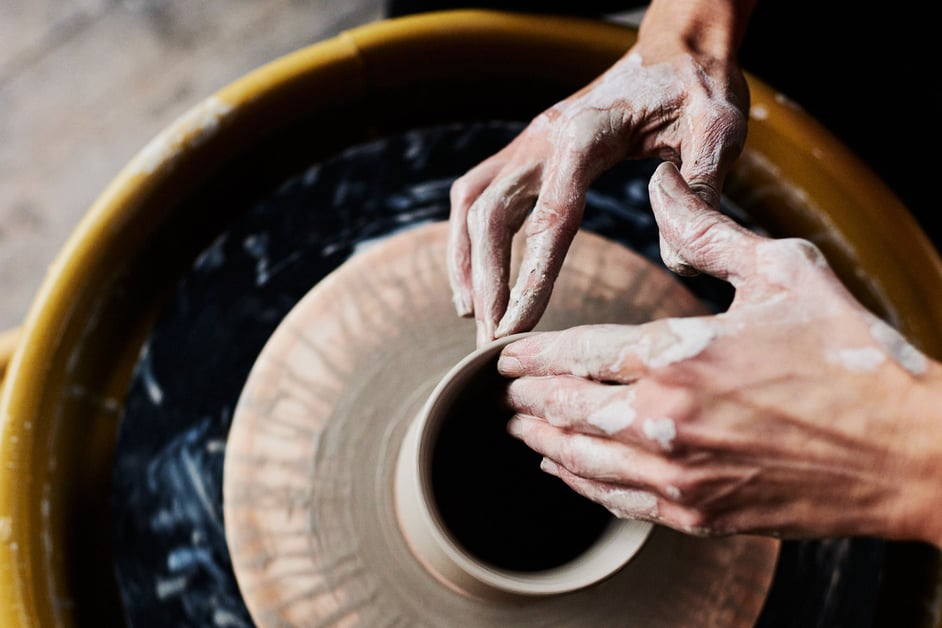 Close-up of a woman's hands as she sculpts a clay pot on a pottery wheel.