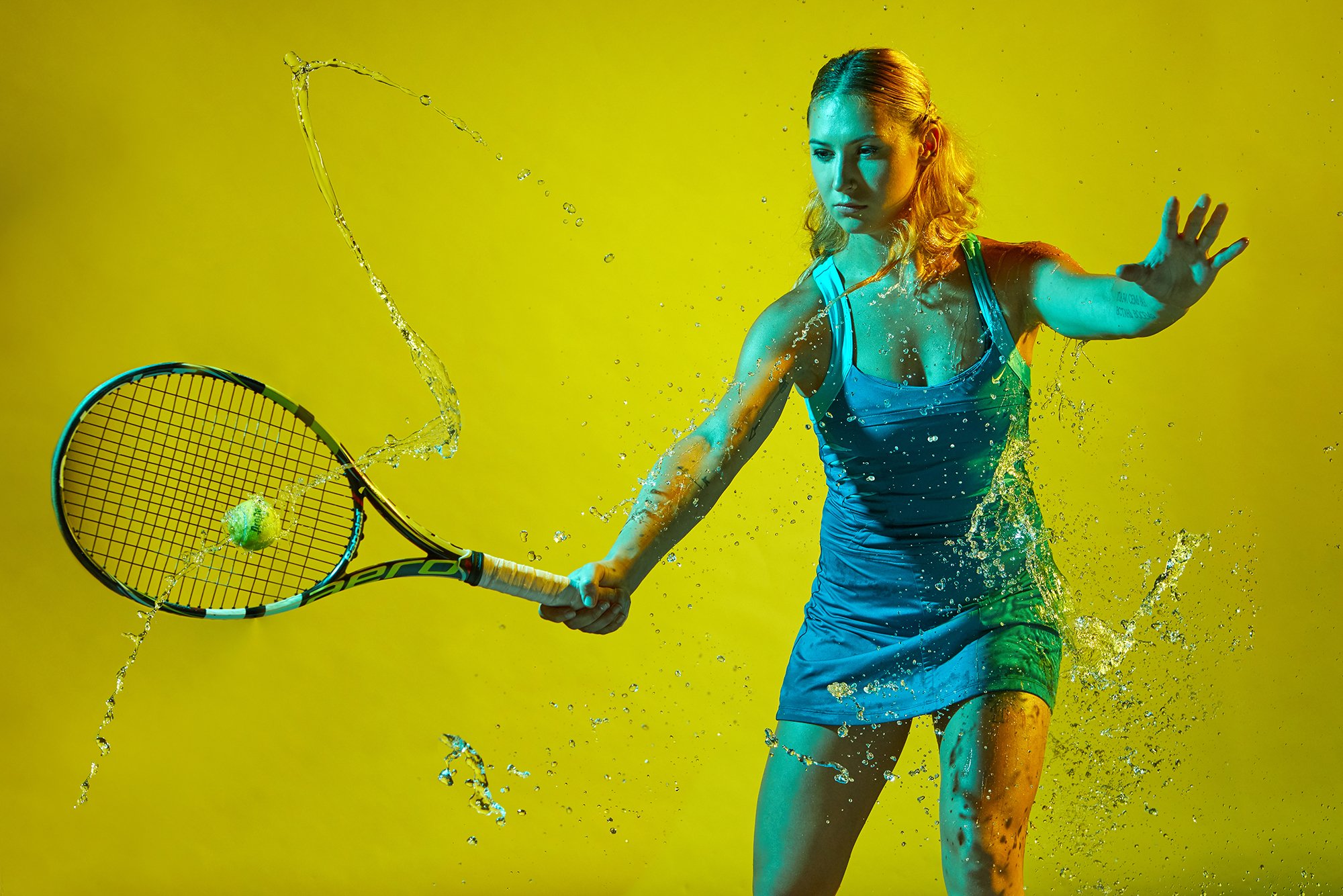 Female tennis player completing forehanded shot while being splashed with water