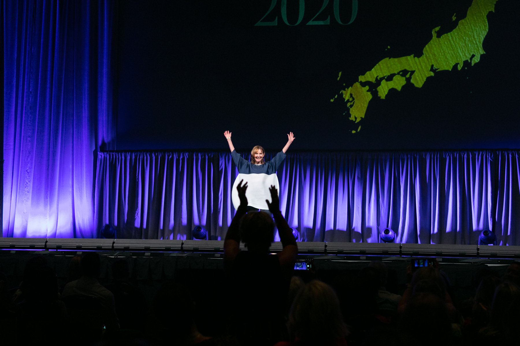Margo Moritz captures a speaker onstage raising her hands in the air, shadowed by an audience member making a similar gesture