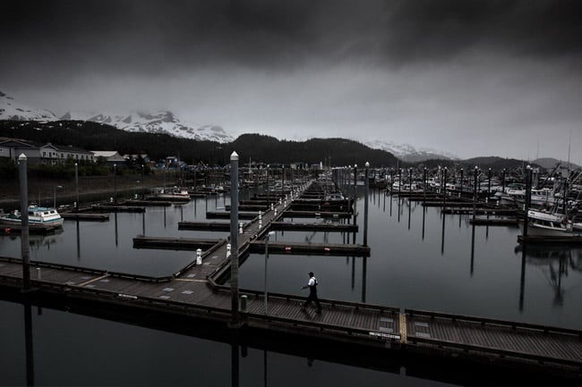 A man walks across a dock and its boats in Cordova, Alaska