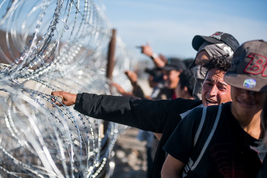 Sean Rayford Image of Central American Migrants walking alongside a barbed wire fence