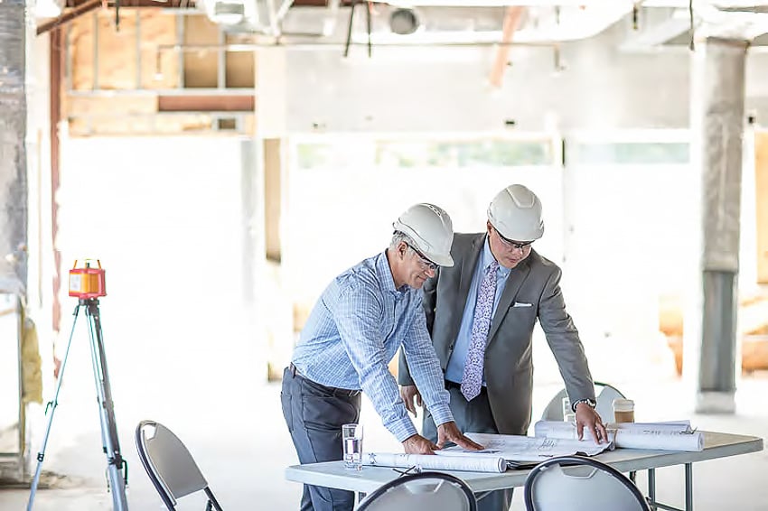 Two men in hard hats on an interior construction site looking at blueprints