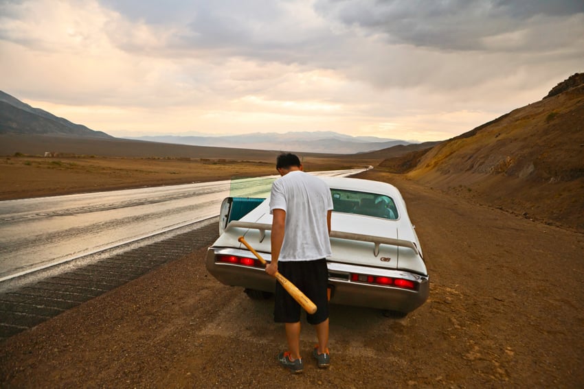 A young man holding a baseball bat is opening the trunk to his car in Death Valley, CA Giacomo Fortunato.