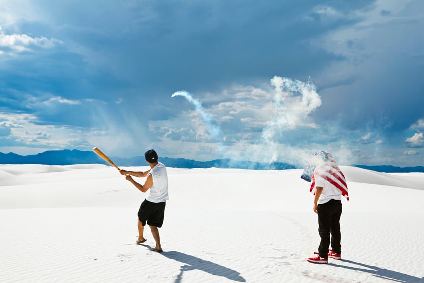 Two young people, one with a baseball bat and the other with an American Flag on his head, hit fireworks into the distance in Death Valley, CA. 