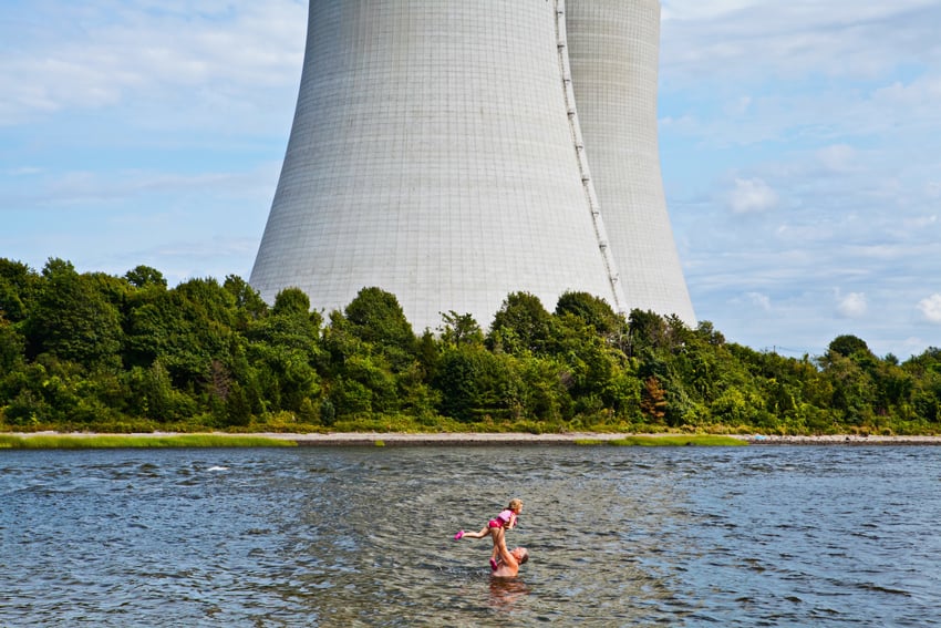 A father plays with his young daughter in a lake in front of a nuclear power plant. 