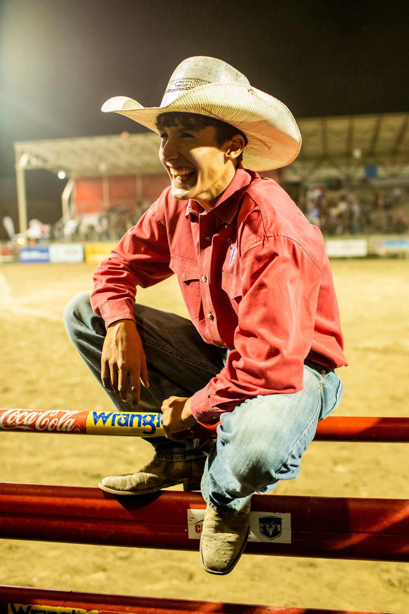 A teen in a cowboy hat perches on the rodeo gate in this portrait by Adam Hester