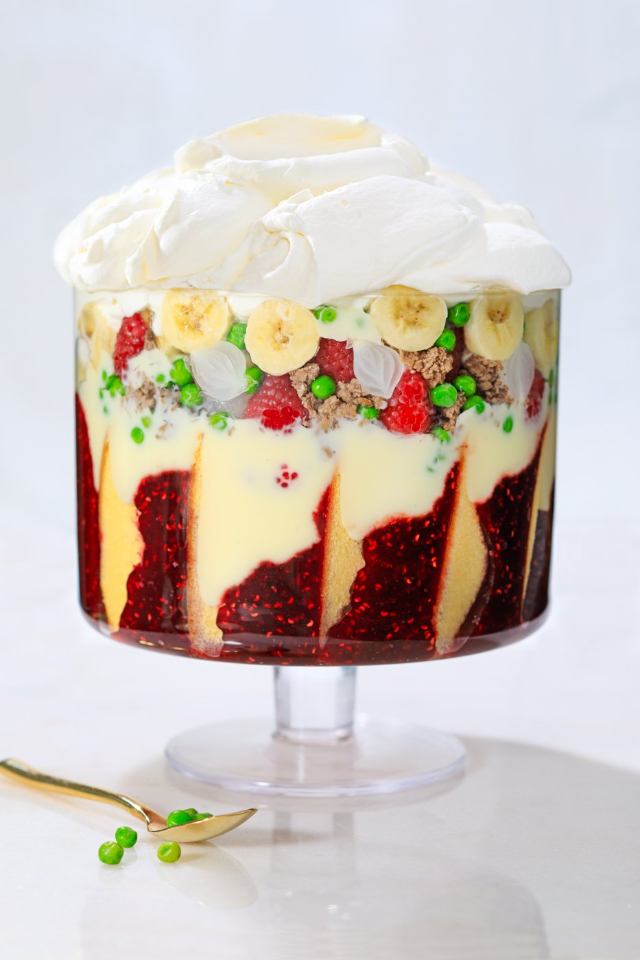 A layered trifle with cake and jam the bottom, cream and fruits in the middle, and topped with whipped cream