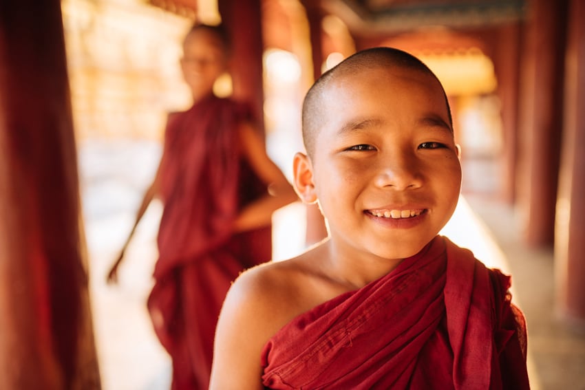 Ben Pipe's portrait from Myanmar of a smiling child monk with a buzzed haircut and red robes.