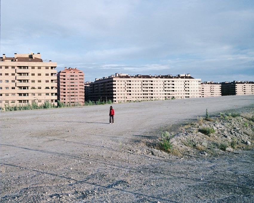A person in a red sweater with massive buildings in the background, shot by Markel Redondo.