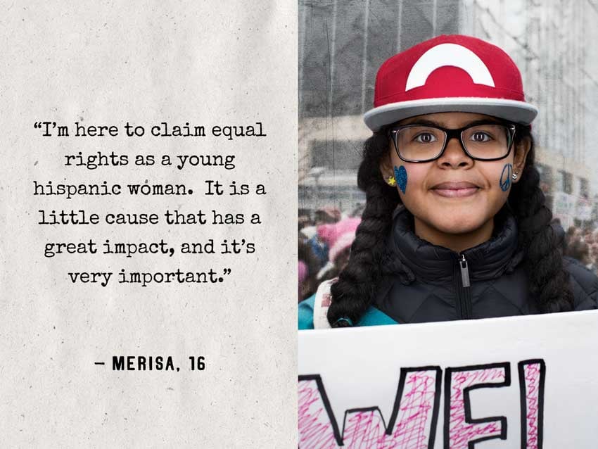An image by photographer Natalia Weedy featuring a girl with her hair in two thick, dark braids holding up a picket sign (out of frame). She wears a red and white baseball cap and thick, dark glasses frames.