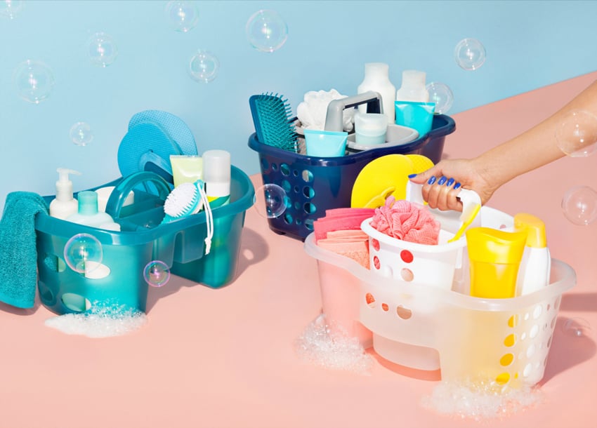 Paul Owen's image for Target featuring three plastic shower caddies surrounded by bubbles in the air on a pink surface with a blue background. The caddies are each filled with various toiletries and no branding or wording on the products are visible.