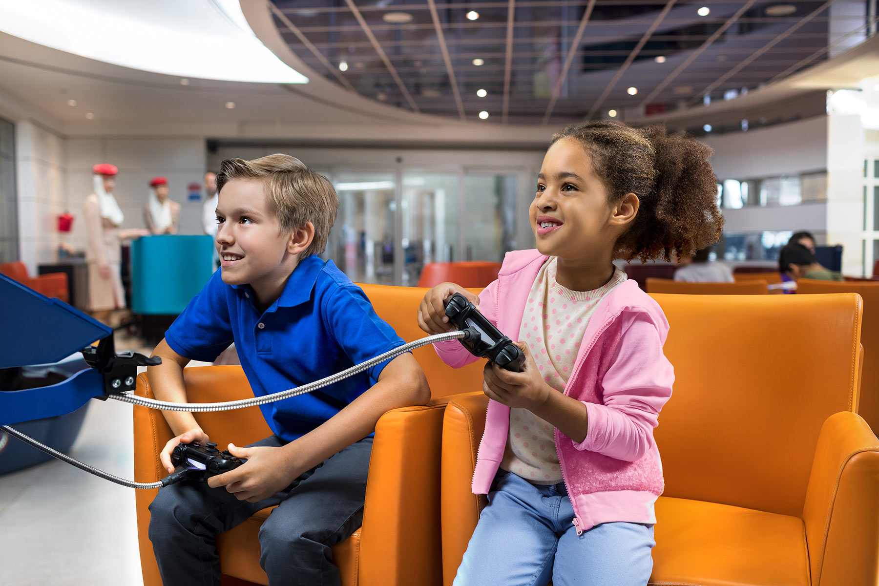 Richard Boll shows two young children on orange chairs with game controllers at Dubai Airport