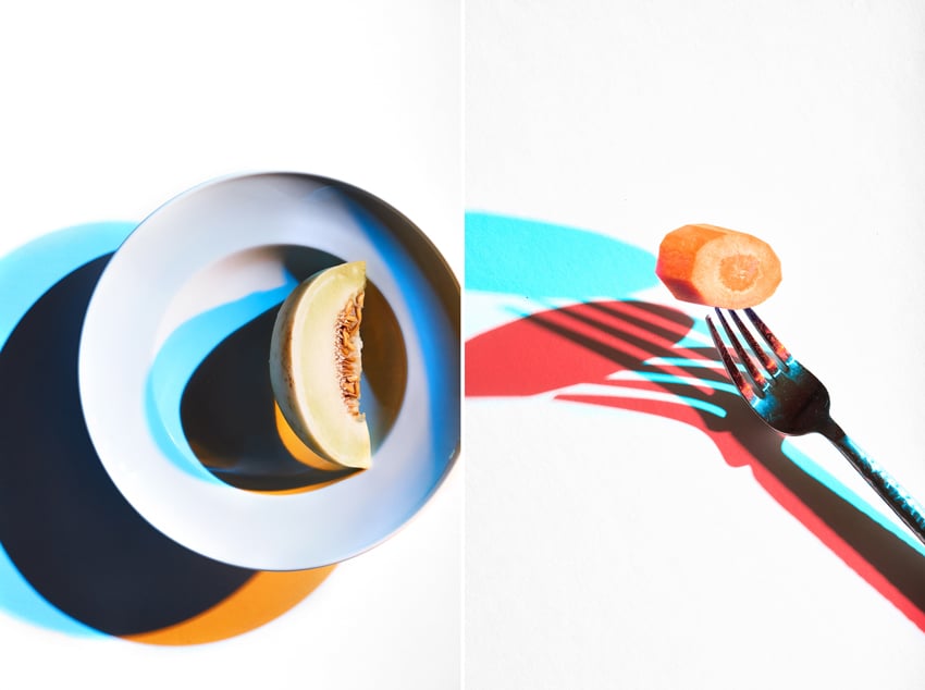A diptych of photos by photographer Shea Evans. On the left is a dish containing one slice of honeydew melon on a white surface. The dish and melon each cast both a teal and orange shadow. On the right is a photo of a slice of a carrot on a fork that casts a teal and red shadow on a white background.
