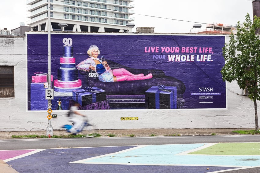 Outdoor building-side mural taken from photo by Clay Cook of  Instagram star Baddie Winkle sipping champagne on a purple sofa  for Stash Investing.