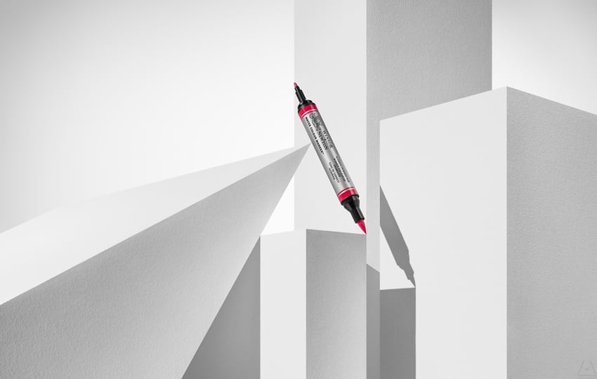 Timothy Hogan's photo for Winsor & Newton featuring a large double-ended red marker with two different gauged tips. It is balanced among several white plinths and casts a shadow. 
