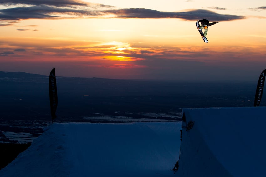 Photographer Adam Moran's photo for Mountain Dew. The photo features a person in the air on a snowboard over a half-pipe. In the background is an orange and red sunset.