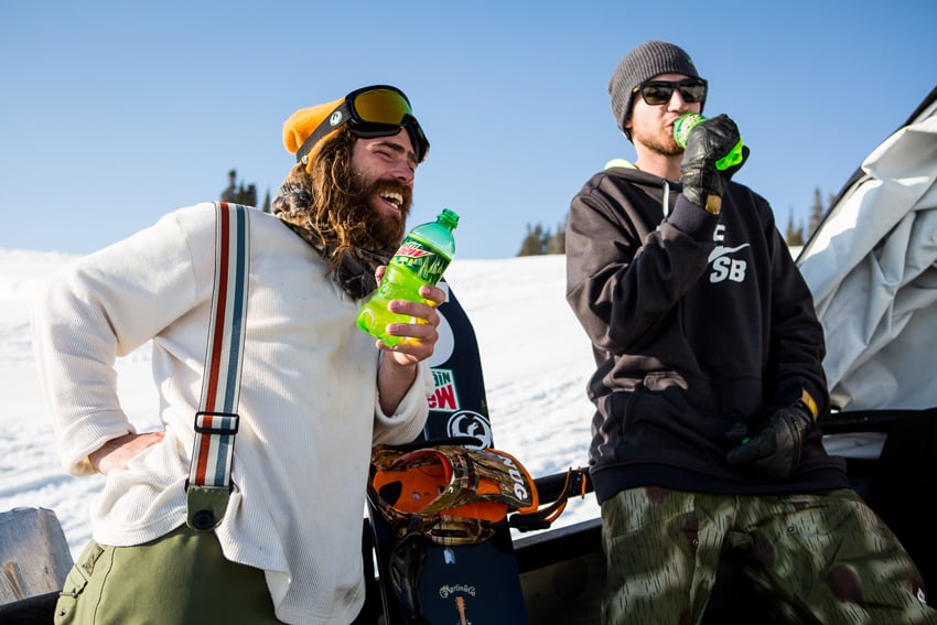 Photographer Adam Moran's photo for Mountain Dew. The photo features two men in snowboarding outfits enjoying Mountain Dew. The man on the left laughs with his hand on his hip, and the man on the right is drinking his Mountain Dew.