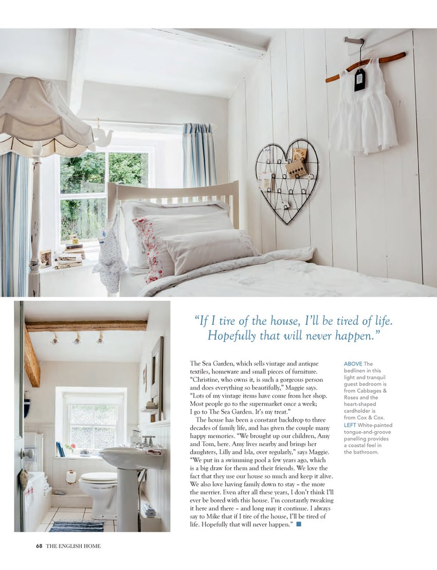 A page from an article in The English Home featuring two photos by Anya Rice of a seventeenth-century home in Cornwall, England. The top photo features a nearly entirely white bedroom with a window, and the bottom photo featured a largely white bathroom with prominent warmly colored wooden beams on the ceiling.