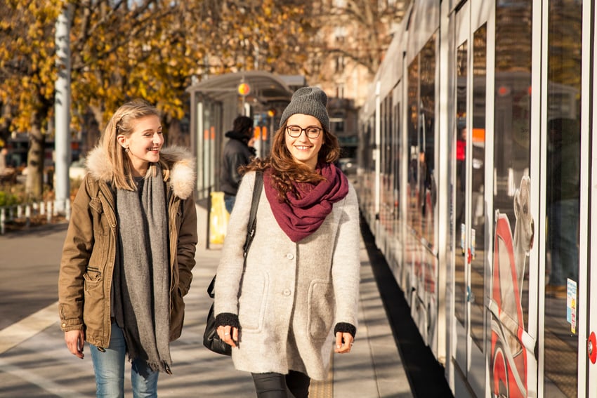 Aurélien Bergot's photograph for Geneva Public Transport featuring two women smiling while walking alongside a bus.