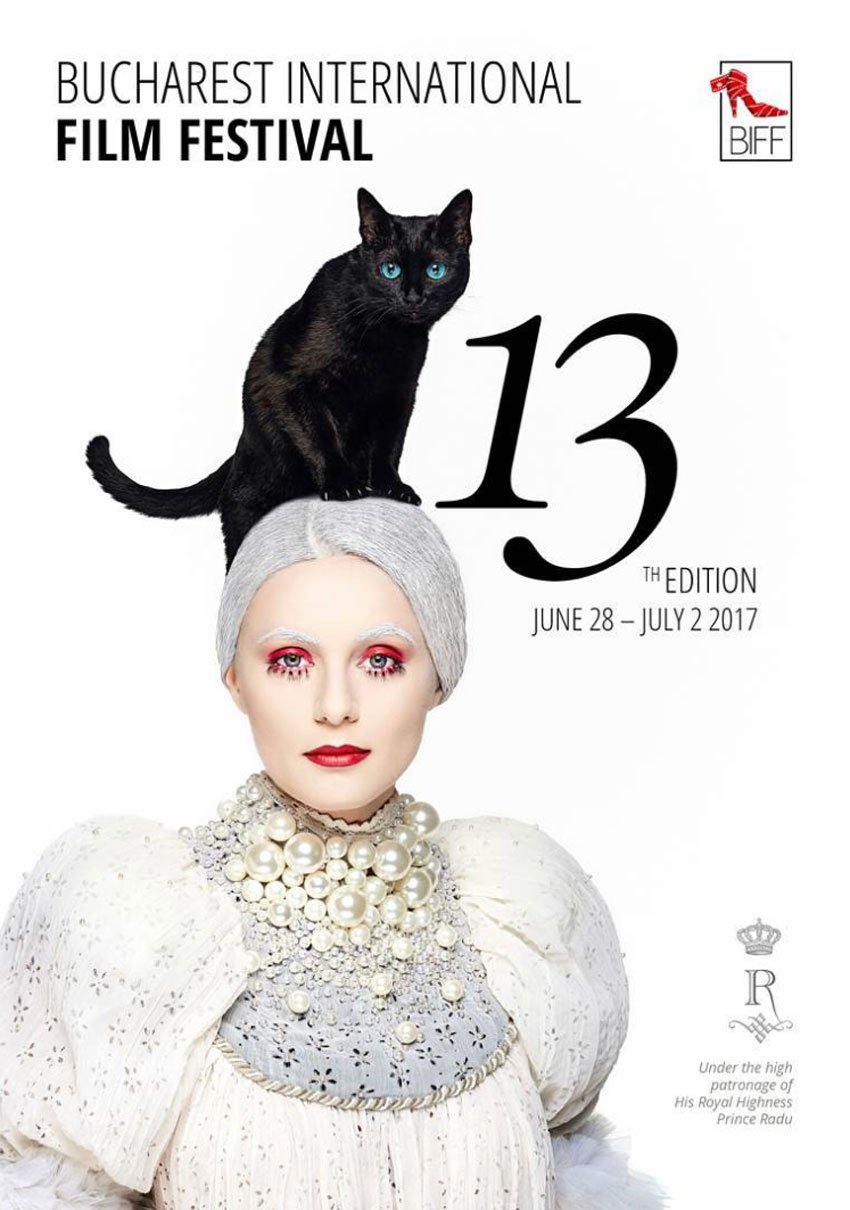A tear sheet for Bucharest International Film Festival featuring photography by Bálinth Hajagos. The photo features a pale woman with blue eyes wearing heavy theatrical makeup. Her hair and eyebrows are powdery white, and she wears a white stylized Elizabethan costume with puffy sleeves. A black cat with vibrant blue eyes is atop her head. 