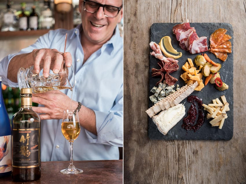 A diptych of photos by C2 Photography for Aspen Sojourner Magazine. On the left is an image of a man smiling as he pours golden liquid into a small stemmed cocktail class. On the right is an image taken from above of a charcuterie board with various meats and cheeses. There are also crackers, pickles, and smears of condiments. The charcuterie board itself is a rectangular piece of thin gray stone. It sits on a weathered wooden tabletop.