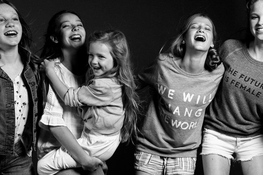 Photographer Caitie McCabe's studio image of five girls. One of the girls hold the smallest child in her arms, and all five appear to be laughing. 