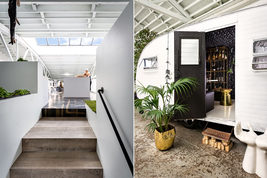 A diptych featuring a pair of photos by Chris Bradley for PROjECT Interiors of the interior of their office space. On the left is a photo featuring 3 broad and deep wooden steps leading up to a space with a large skylight. The photo features pops of green from ornamental plants and greenery. On the right is an image featuring a white old-fashioned trailer that itself sits inside a larger open space within the office. The trailer's door is open and there is a small palm to the left of the open door in a shiny brass planter. To the right of the open door is a white sculpture of 2 human hands that a person could use as a seat.