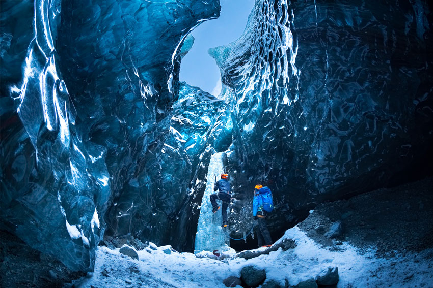 A man climbing out of an icy cave, photo by Clark Vandergrift.