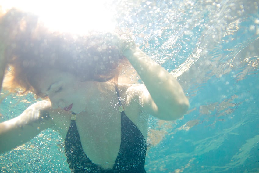 Claus Lehmann's photo of a woman underwater. She wears a black bathing suit with gold-toned details and red lipstick. Her red hair is suspended in the water around her face.