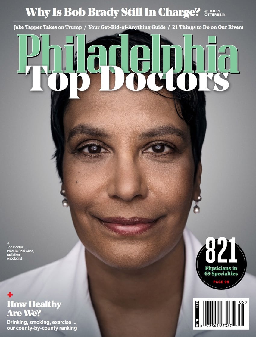 A headshot of Dr. Pramila Rani Anne, a radiation oncologist, by photographer Colin M. Lenton for the cover of Philadelphia Magazine. Pramila is a woman of color. She wears a white doctor's coat, small dangling pearl earrings, and a subtle rosy lip color. She has a short pixie haircut.