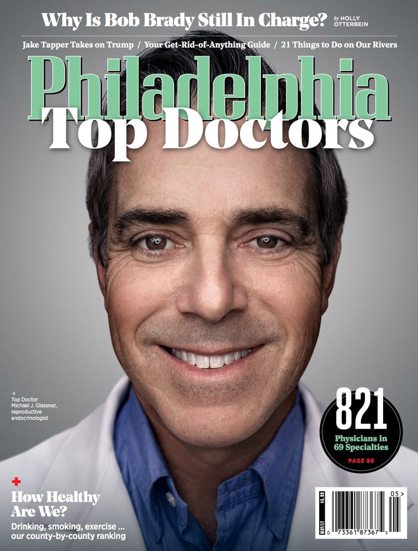 A headshot of Dr. Michael J. Glassner, a reproductive endocrinologist, by photographer Colin M. Lenton for the cover of Philadelphia Magazine. Michael is white and smiles showing his teeth. He has brown eyes and wears a blue collared shirt that is unbuttoned at the top button and a white doctor's coat.