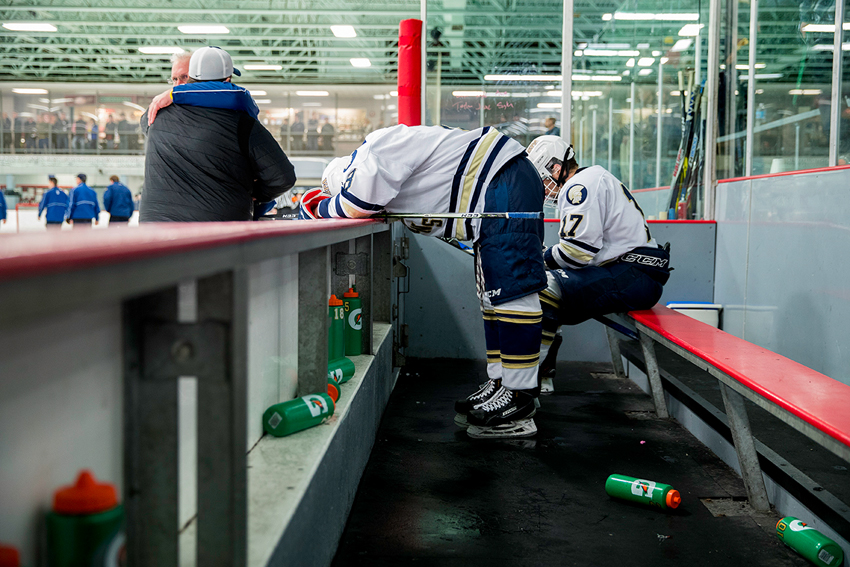 Photographer David Ellis' photo of two ice hockey players on the sidelines. Gatorade brand plastic water bottles are strewn about, and one of the two players leans over the wall with his face buried in his arms.