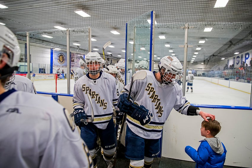 Photographer David Ellis' image of the Spartans, a high school ice hockey team, leaving the ice. The first boy exiting the ice scratches a little boy in a blue puffer coat affectionately on the head.