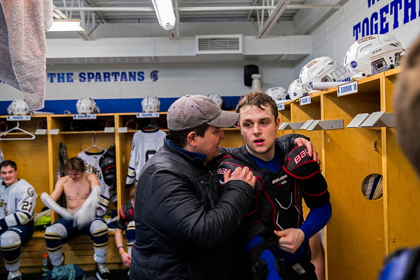 Photographer David Ellis' image from the Spartan's team locker room of an adult man comforting one of the hockey players by grabbing his shoulder. The athlete is sweaty and looks tired.