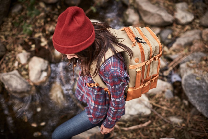 An image captured by photographer David Troyer for Eagle Creek of a woman wearing an Eagle Creek backpack. The photo is taken from above. She wears a blue, red, and white flannel button-down shirt and a maroon beanie, and she has long dark brown hair.