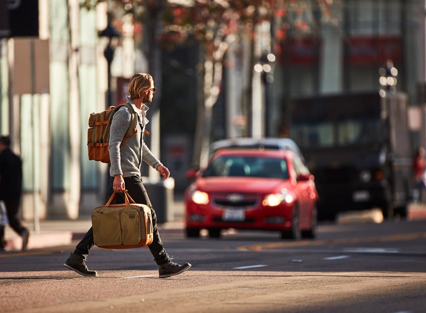 Photographer David Troyer's photo for Eagle Creek featuring a man with blonde hair crossing a street wearing an Eagle Creek backpack and carrying an Eagle Creek bag in his right hand. 