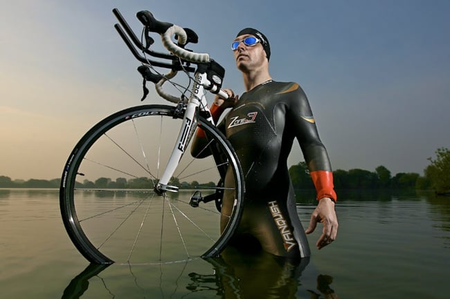 Dom Romney captures a tri-athlete in a wetsuit, cap and goggles carrying a bike on his shoulder while in the water