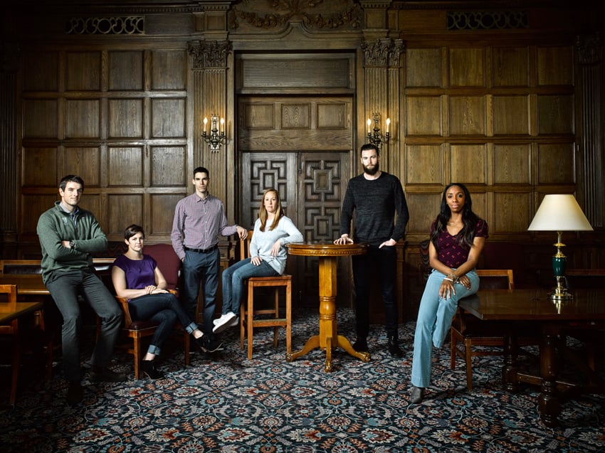 A portrait of six Olympians by photographer Doug Levy for Financial Times. The six people are sitting and standing in a carpeted room with wood paneled walls.
