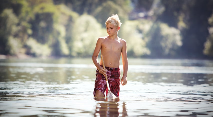 Boy with a fishing net in his hand looking for fish in a lake.