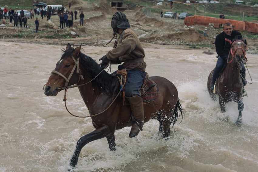 Buzkashi riders wading through a shallow river shot by Marc Ressang