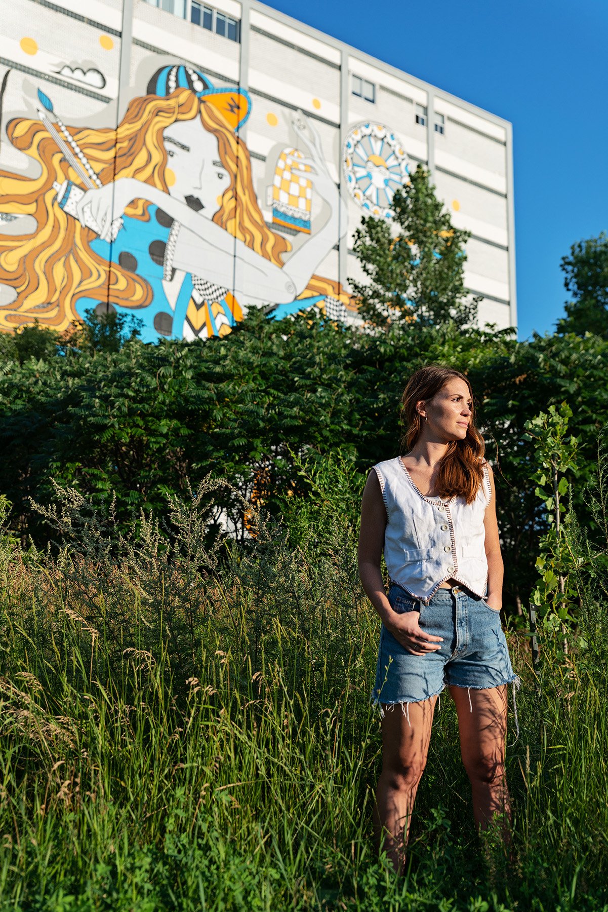 Brittany stands in front of greenery and another mural in Mile End in this photo by David Giral