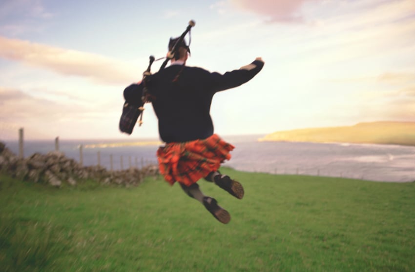 A Scottish bagpiper jumping with The Isle of Skye in the background, photo by Eric Schmidt