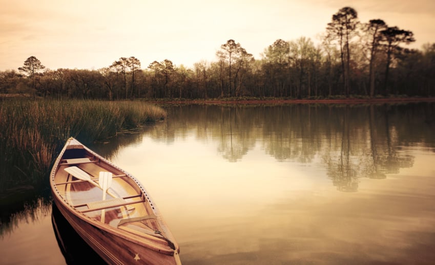 A shot of an empty canoe on a still lake with trees in the background, photo by Eric Schmidt