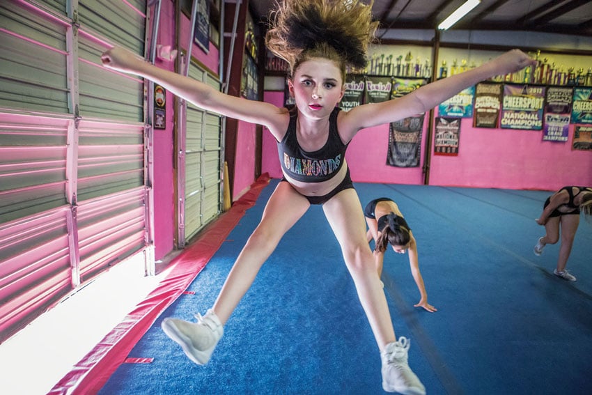 a photo of a young cheerleader focusing intently as she practices her jump, her determination palpable against the backdrop of the gymnasium, photo by Felix Sanchez.