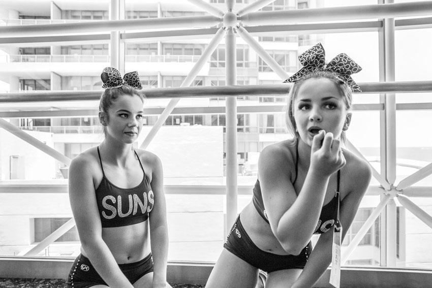 Two teenage cheerleaders delicately apply makeup, their focused expressions reflecting the anticipation and excitement building before the show.