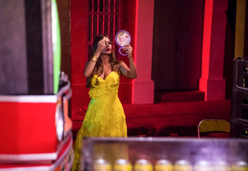 A photo by Fernando Decillis of Sofia Vergara in a bright yellow dress fixing her makeup using a small handheld mirror.